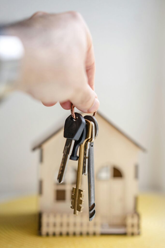 A person holding house keys in front of a house model. 